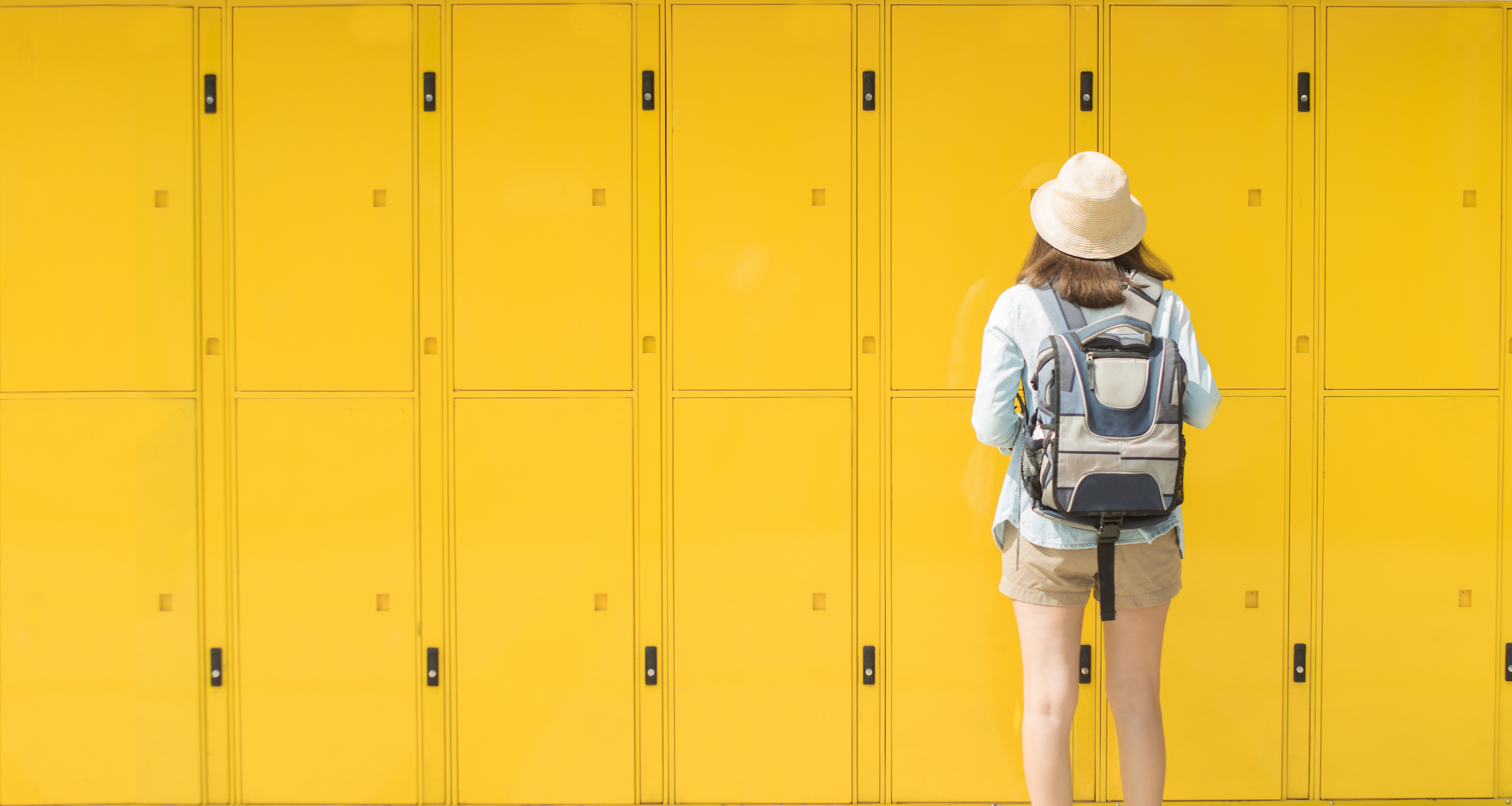 Image of a young woman standing in front of a wall of yellow lockers